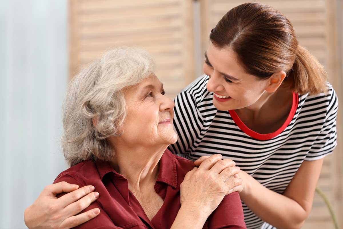 elderly woman sitting at home and smiling while receiving comfort from a hospice volunteer