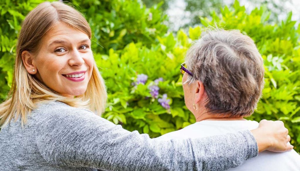 smiling hospice caregiver with elderly woman on bench overlooking beautiful greenery