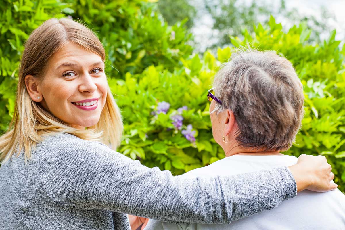 smiling hospice caregiver with elderly woman on bench overlooking beautiful greenery